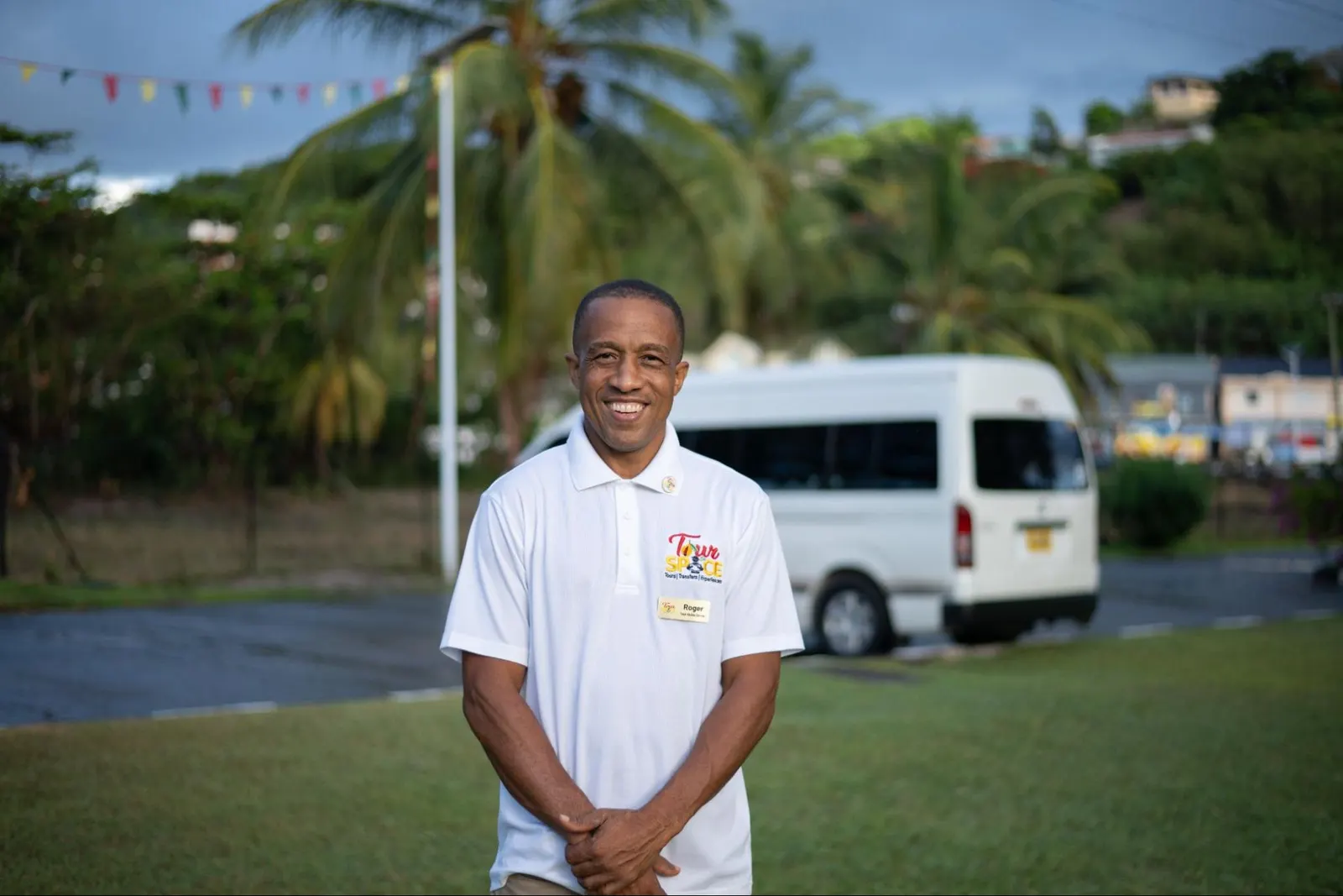 Roger, Tour De Spice history guide, smiling beside a tour van in Grenada